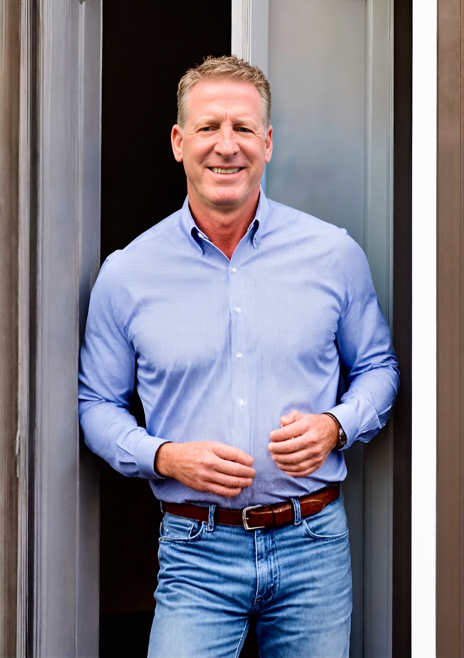 Jeff in a button down and jeans standing in front of a building.